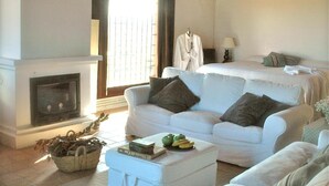 A spacious living room with a fireplace, white sofas, and a large window. - Mas del Mar (Sant Pere Pescador)