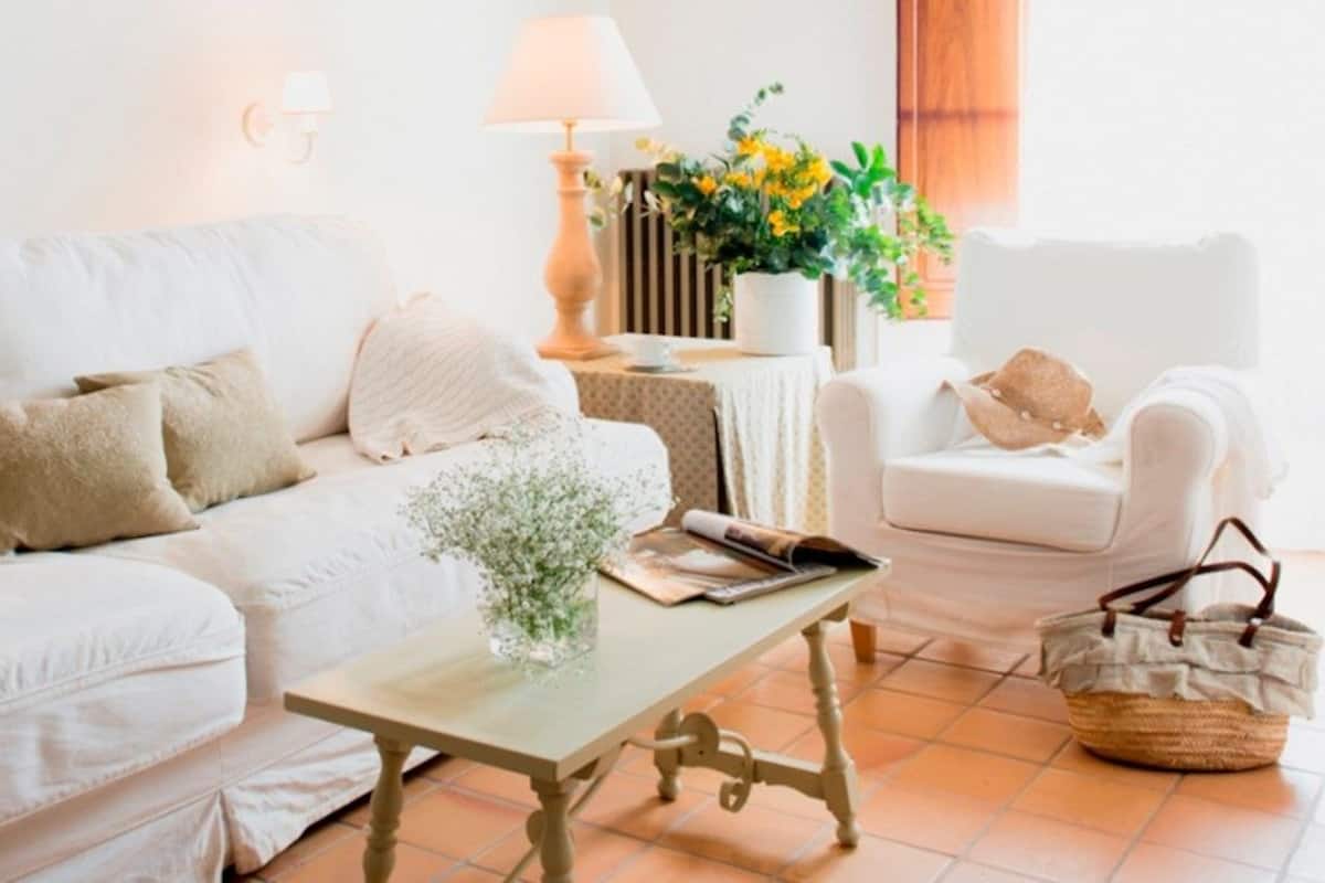 Een woonkamer met een witte bank, een salontafel, een witte fauteuil, een lamp en een plant in een pot.