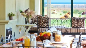 A breakfast table with fruit, a coffee pot, and a view of cattle grazing by the ocean. - Mas del Mar (Sant Pere Pescador)