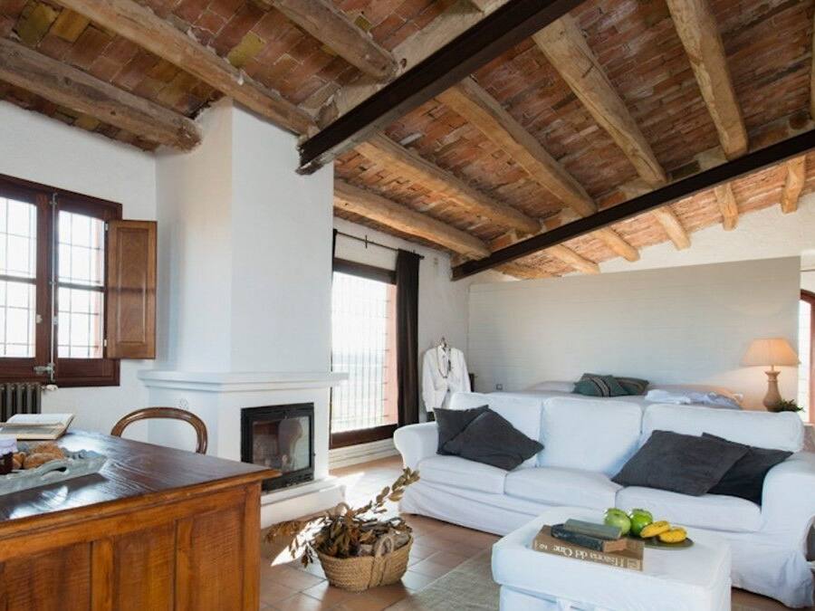 A cozy living room with a fireplace, white sofa, wooden dining table, and a rustic ceiling.