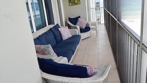 Un balcón con sofás y sillones de mimbre, una pared decorativa y vista al mar.