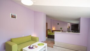 Un salón con un sofá verde, una mesa de centro blanca y una cocina al fondo.