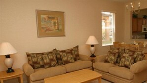 A living room with two sofas, a coffee table, and lamps. There is a painting on the wall and a window with blinds. - Regal Palms Spa & Resort (Davenport)
