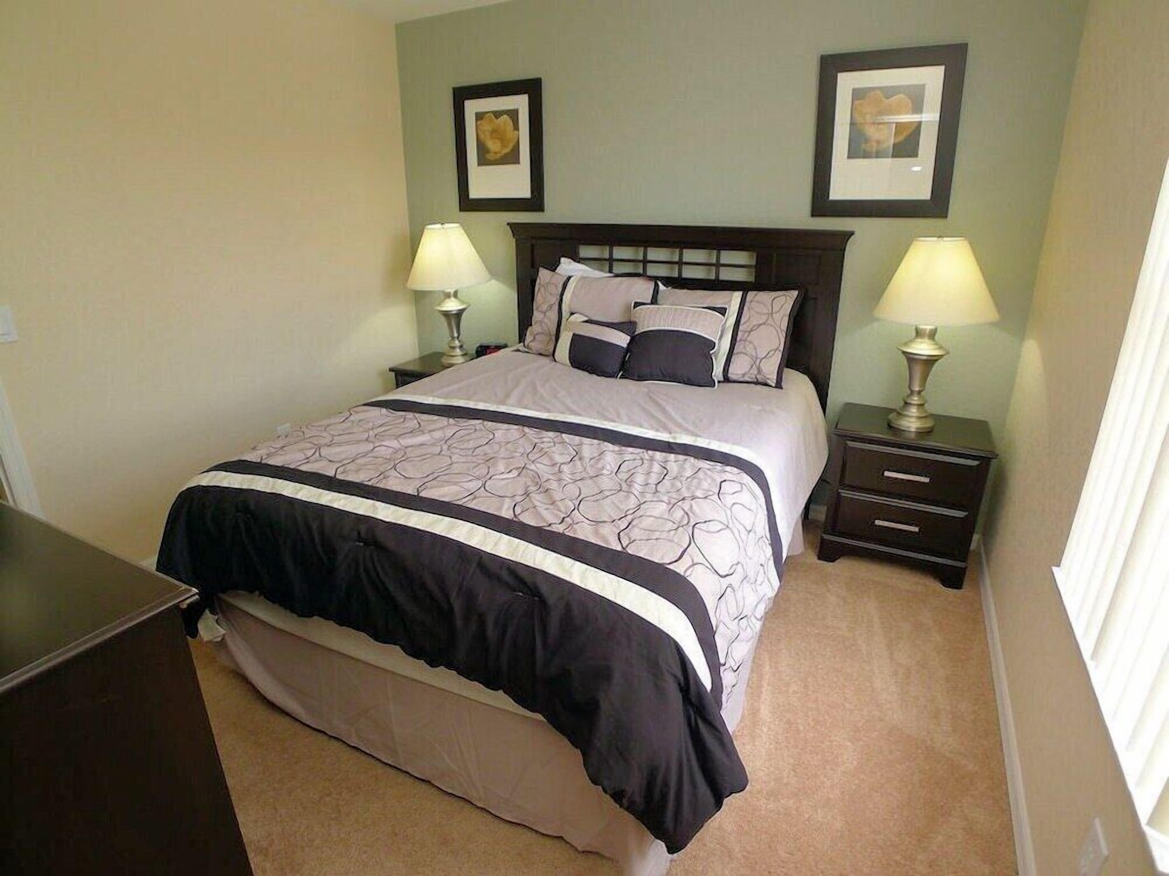 A neatly made bed with a patterned bedspread, two bedside lamps, a nightstand with drawers, and two framed pictures on the wall.