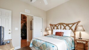 A bedroom with a bed, two bedside tables, a television, and a door leading to another room. - Regal Palms Spa & Resort (Davenport)