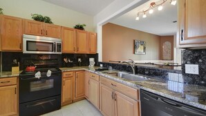 A kitchen with wooden cabinets, a stainless steel stove, a microwave, and a granite countertop. - Regal Palms Spa & Resort (Davenport)