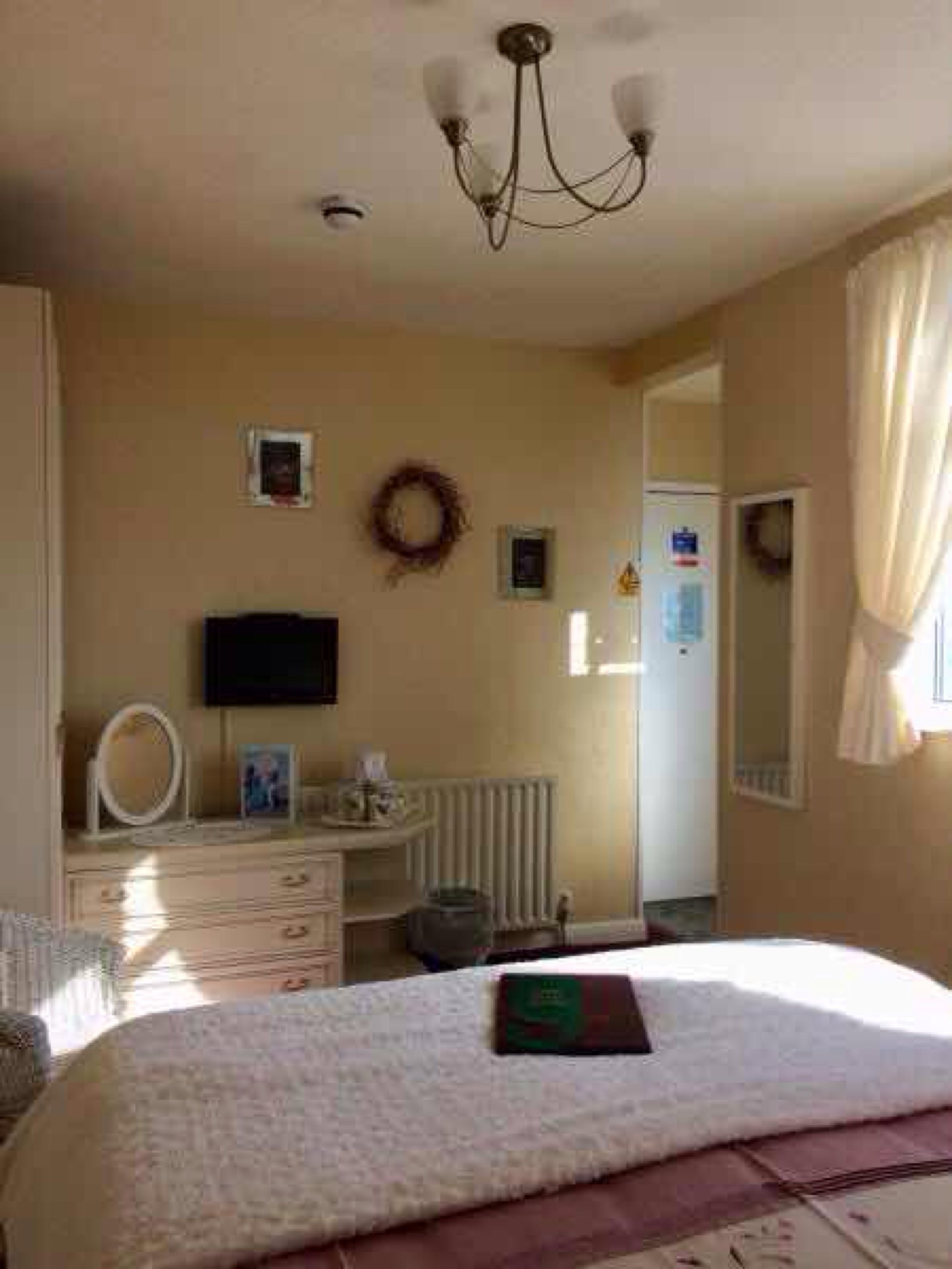 Une chambre à coucher comprenant un lit, une commode, un miroir, un téléviseur et un radiateur.