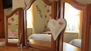 A bedroom with a wooden floor, a bed with white bedding, a heart-shaped mirror, and a small vase with reed sticks. - The Sunningdale (Skegness)
