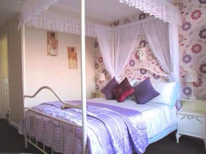 A bedroom with a four-poster bed, floral wallpaper, and a nightstand. - The Sunningdale (Skegness)