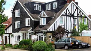 A traditional black and white Tudor-style building with a corner entrance, a visible shop on the ground floor, and a parked car in front. - The Sunningdale (Skegness)