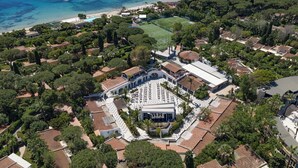 An aerial view of a coastal residential area with a central building surrounded by trees and a beach.