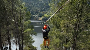 A person bungee jumping with a harness and helmet, surrounded by trees and a body of water. - Forte Village Resort - Le Dune (Pula)