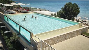 A rectangular pool with clear water, surrounded by lounge chairs and umbrellas, overlooking a calm sea.