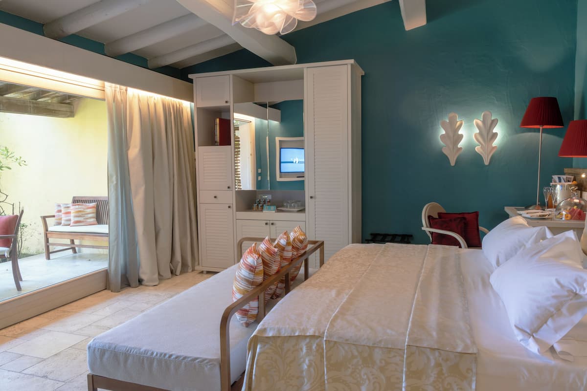 A bedroom with a bed, a desk, a chair, a wardrobe, and a large window with curtains.