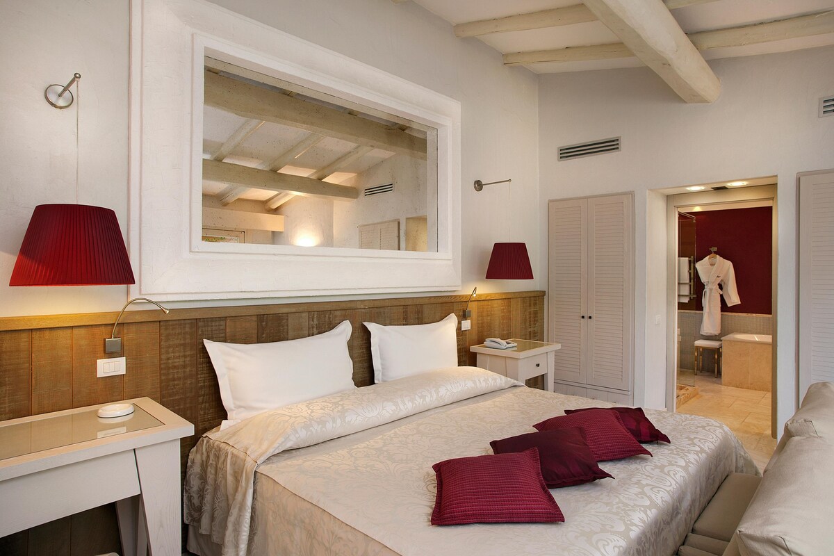 Camera d'albergo con un letto grande, due comodini, uno specchio e un armadio.