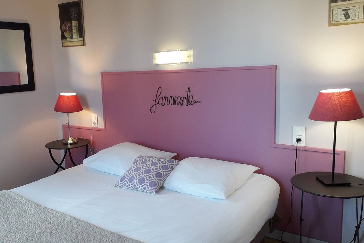 A hotel room with a bed, two bedside tables with lamps, a mirror, and a decorative wall piece.