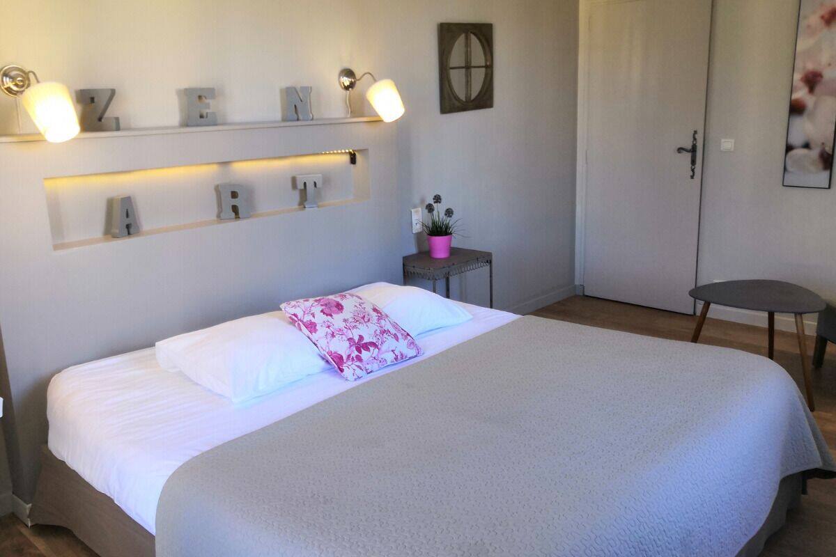 A neatly arranged bedroom with a bed, bedside tables, and a wall-mounted shelf with illuminated letters.
