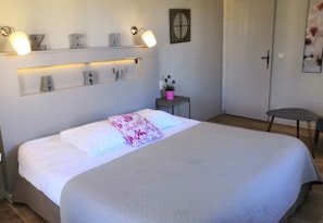 Ein ordentlich eingerichtetes Schlafzimmer mit einem Bett, Nachttischen und einem an der Wand befestigten Regal mit beleuchteten Buchstaben.