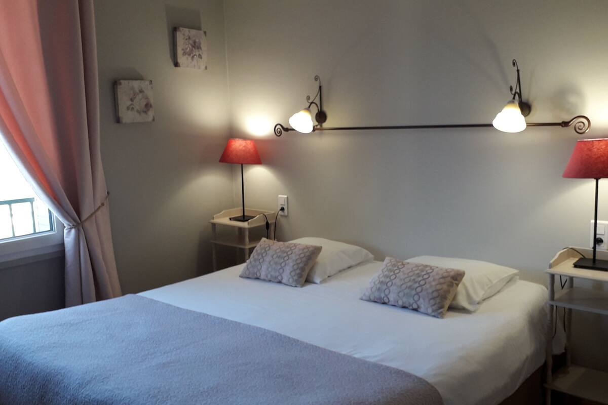 A neatly made bed with two pillows, a bedside table with a lamp, and a wall-mounted light fixture.