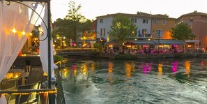 Un restaurante a la orilla del río con terraza y vistas a edificios al otro lado del agua.