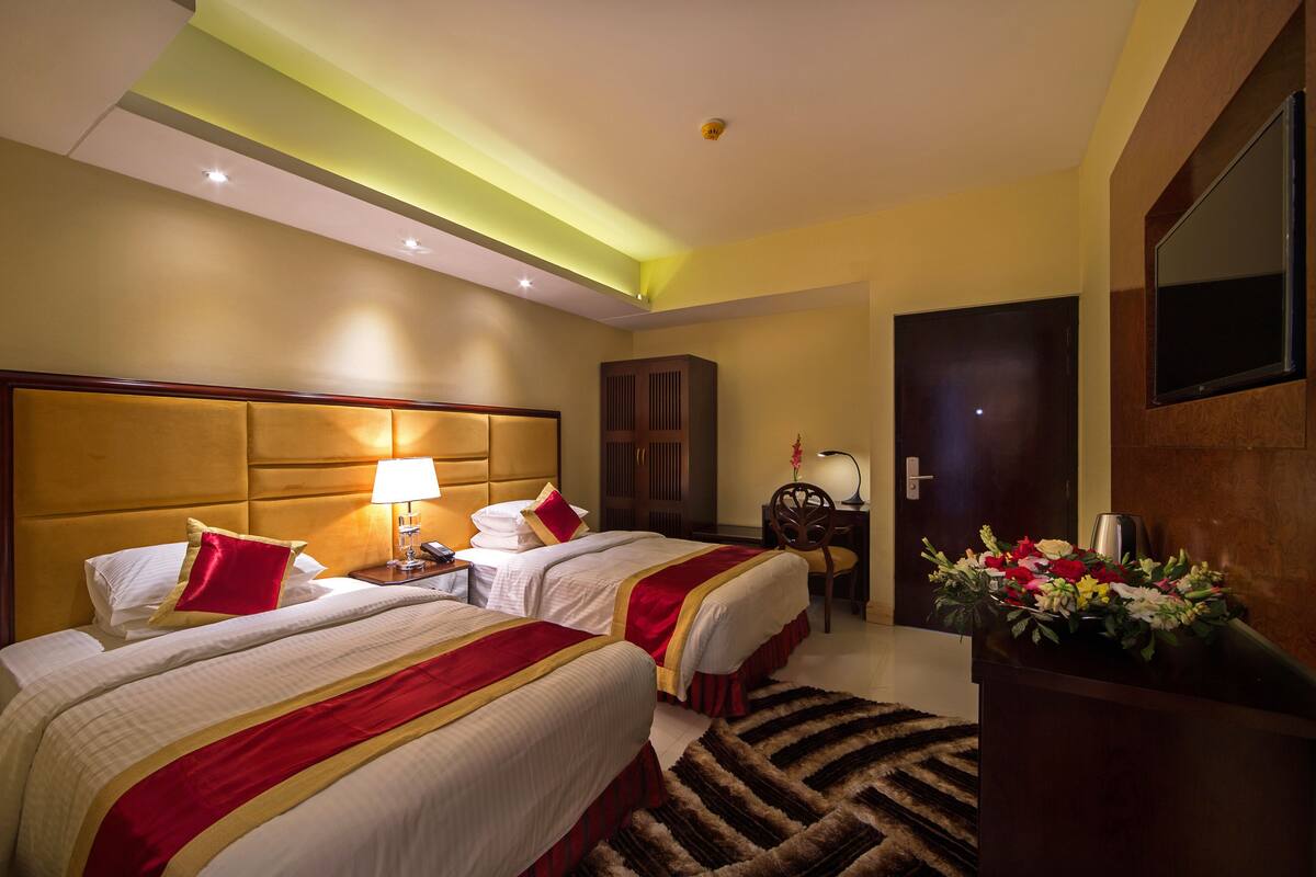Habitación de hotel con dos camas, un escritorio, una silla, un televisor y un arreglo floral.