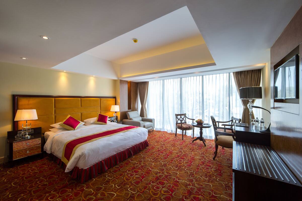 Habitación de hotel con una cama grande, un escritorio con silla, un televisor y una ventana con cortinas.