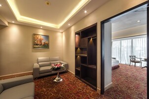 Habitación de hotel con sofá, una pequeña mesa con flores, estantería y cama con vistas al exterior.