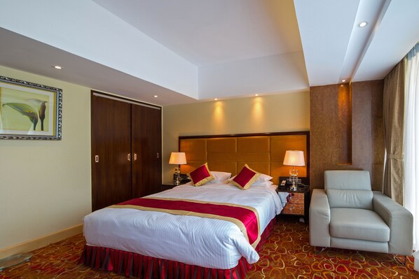 Une chambre d’hôtel avec un grand lit, deux tables de chevet avec des lampes, une chaise, une armoire et un tableau au mur.