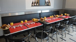 Un restaurant avec de nombreuses tables, chacune recouverte d’une nappe rouge et mise avec des assiettes, des couverts et des verres de jus d’orange.
