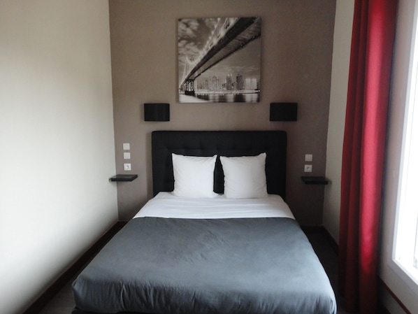 Una cama bien tendida con ropa de cama blanca y gris, un cabecero negro y dos mesitas de noche con lámparas negras.