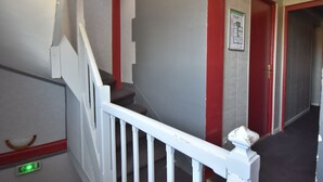 Un escalier avec une rampe blanche, une porte rouge et un panneau vert indiquant la sortie de secours.
