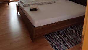 Makuuhuoneessa on puinen sänky, punainen tuoli, pieni pöytä ja ikkuna, jossa on verhot.