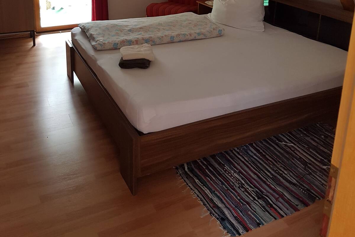 A bedroom with a wooden bed, a red chair, a small table, and a window with curtains.