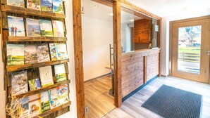 Un área de recepción con un mostrador de madera, un expositor de folletos en la pared y vistas al exterior a través de una puerta de cristal.