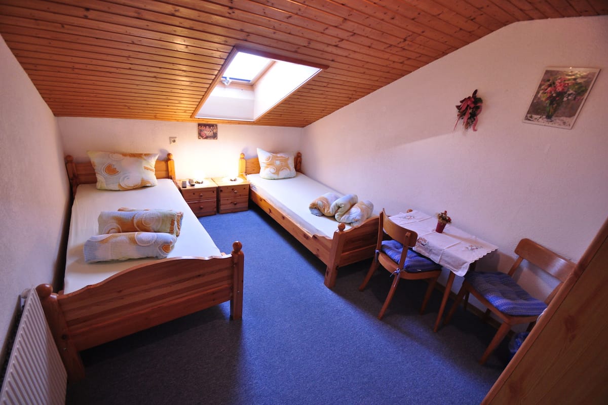 A small, cozy room with two single beds, a wooden table with chairs, a small desk, and a skylight.