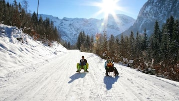 A snowy mountain road with two people sitting on sleds.