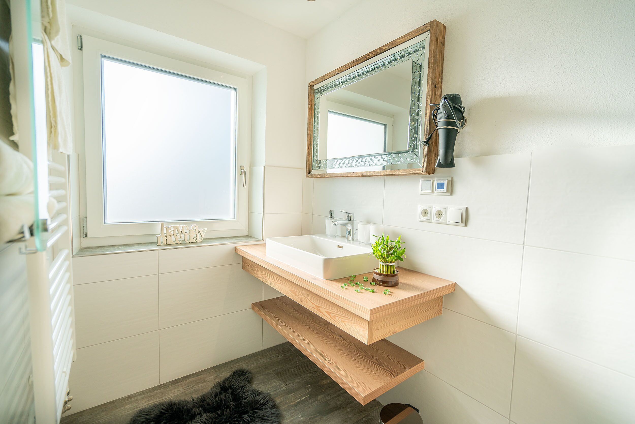 Ein modernes Badezimmer mit einem schwebenden Waschtisch, einem großen Spiegel und einem Fenster.