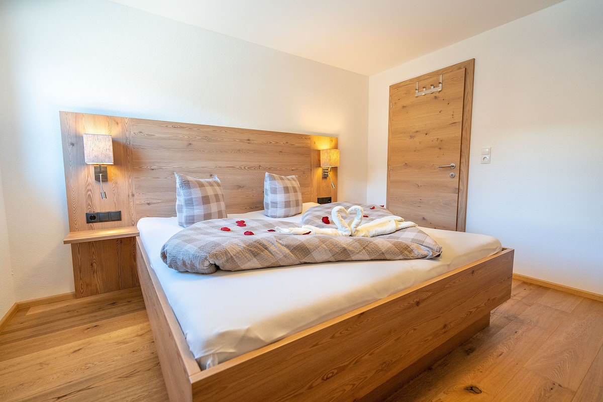 A wooden bed with a headboard, bedside lamps, and a wooden door.