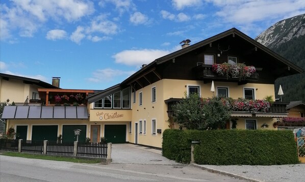 A two-story building with a sign reading "Haus Christlun". It features balconies with flower boxes, a wooden facade, and a mountain backdrop. - Ferienhaus Christlum (Achenkirch)