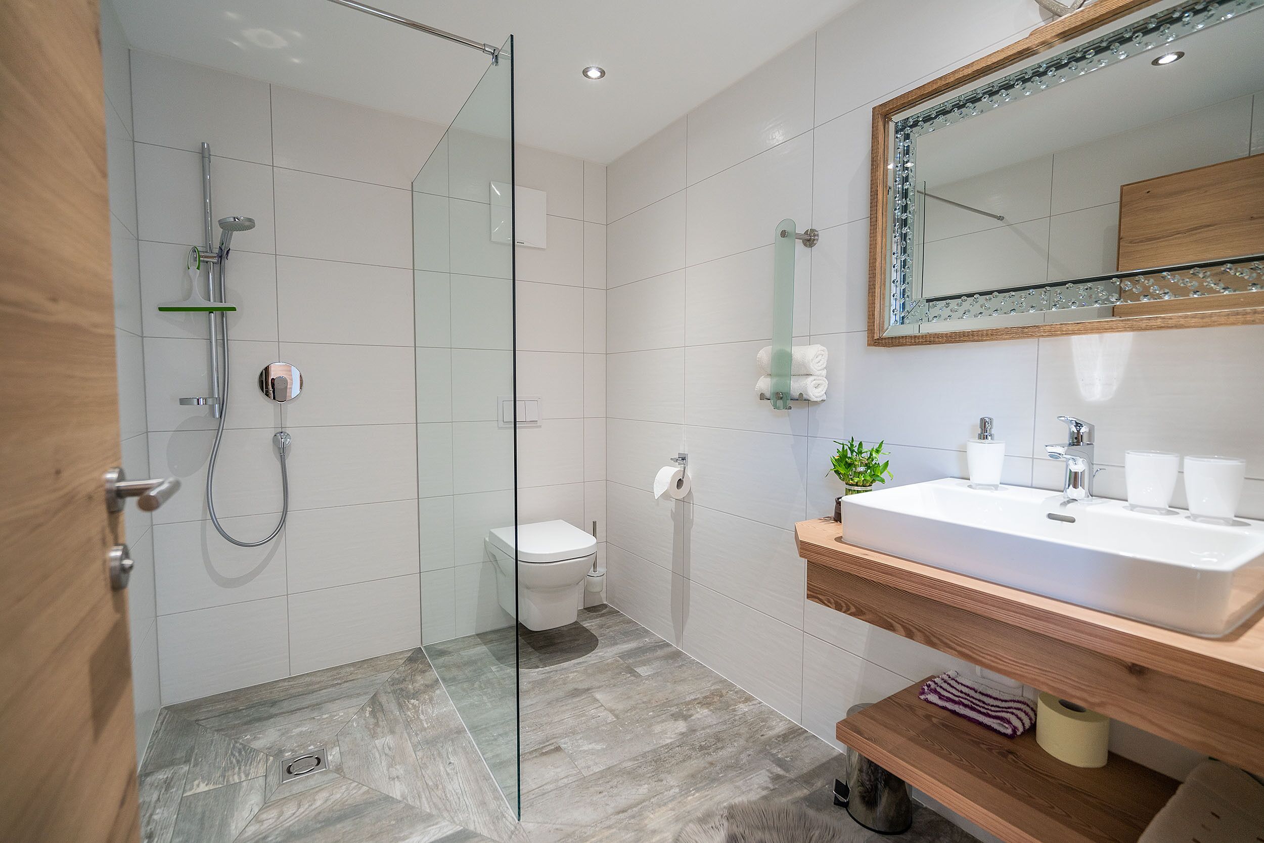 Un baño moderno con cabina de ducha de vidrio, inodoro, lavamanos con espejo y estantes de madera.