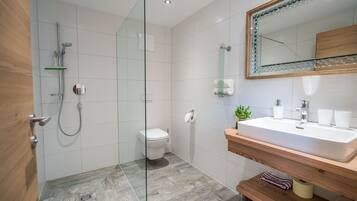 Un baño moderno con cabina de ducha de vidrio, inodoro, lavamanos con espejo y estantes de madera.