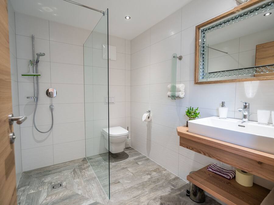 Un baño moderno con cabina de ducha de vidrio, inodoro, lavamanos con espejo y estantes de madera.