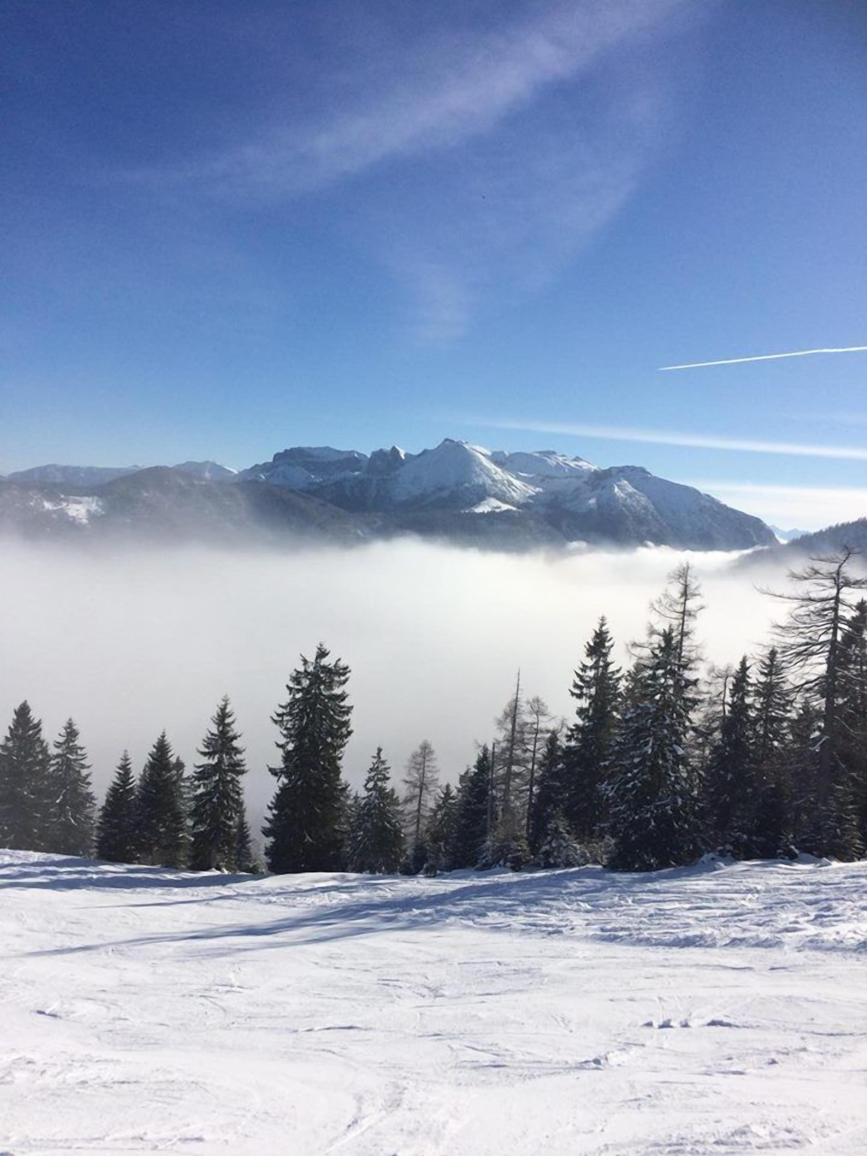 Paisagem montanhosa coberta de neve, céu claro e um rastro de condensação visível.