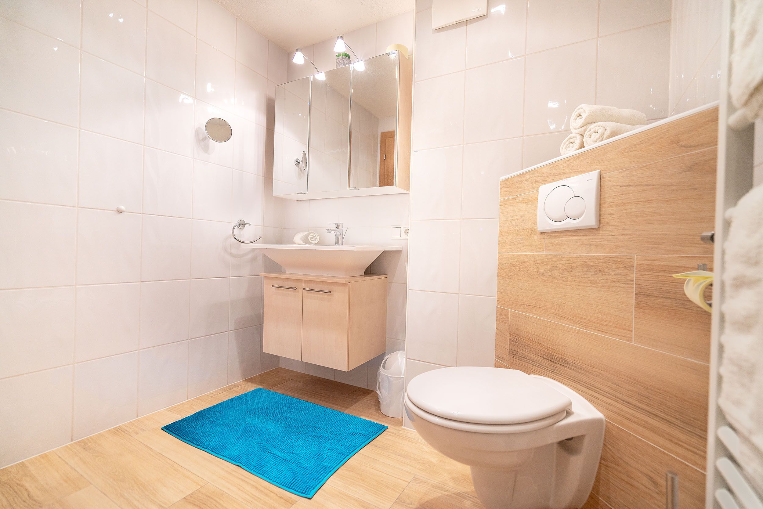 A modern bathroom with a white toilet, a sink with a mirror above, and a blue rug on the floor.