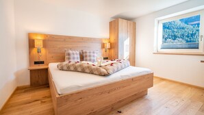 Un dormitorio con una cama de madera, dos lámparas de noche, una ventana con vistas a un bosque y un cuadro en la pared.