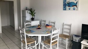 Ein Essbereich mit einem weißen Tisch und Stühlen, einem Bild von Fischen an der Wand, einem Kühlschrank und einer Pflanze.