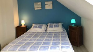 Ein Schlafzimmer mit blauer Wand, einem Bett mit gemustertem Überwurf, zwei Nachttischen mit Lampen und zwei an der Wand befestigten Bildern.