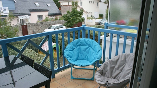 Ein Balkon mit blauer Geländer, einem blauen Stuhl, einem grauen Stuhl und einem Tisch.