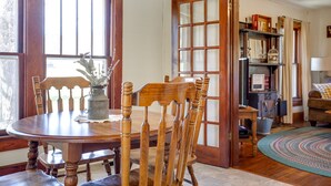 Uma sala de jantar com uma mesa e cadeiras de madeira, um vaso com flores e uma estante de livros ao fundo.