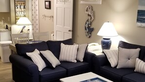 A living room with a dark blue sofa set, a white coffee table, and a white cabinet. There is a ceiling fan, a wall-mounted air conditioner, and a framed picture on the wall. - Welcome to "Ocean Sunrise". Renovated direct ocean front private end unit.  (Wildwood Crest)